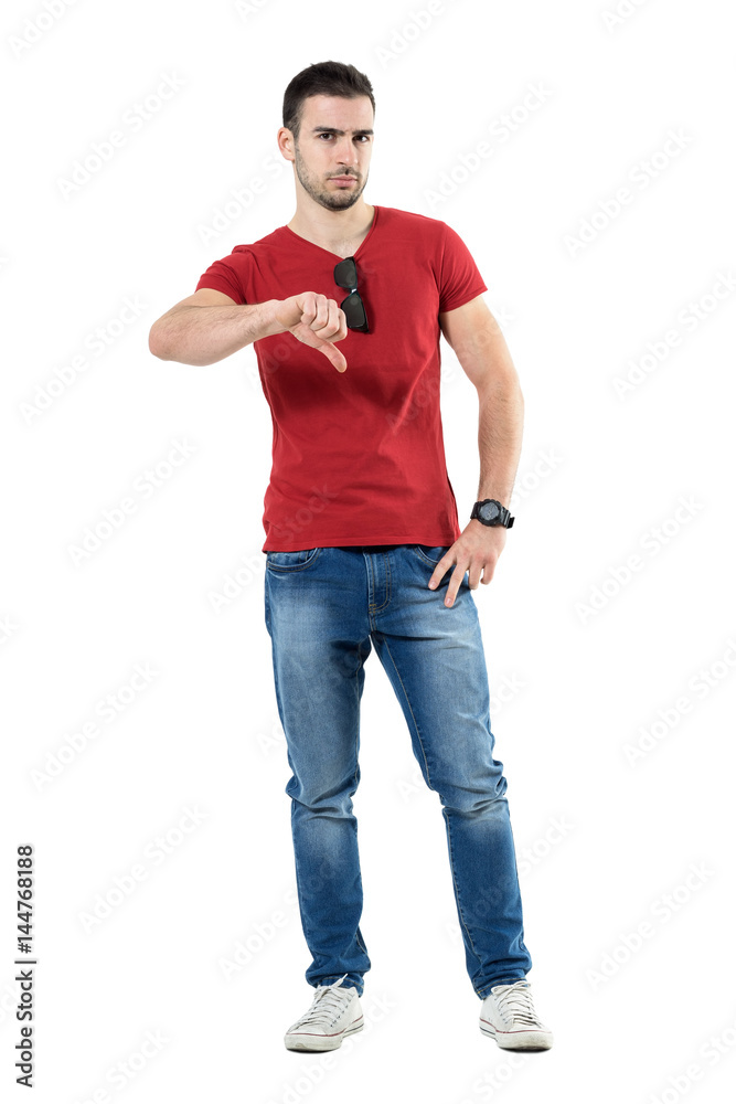 Upset angry young casual man showing thumbs down gesture. Full body length portrait isolated over white studio background. Upset angry young casual man showing thumbs down gesture. Full body length portrait isolated over white studio background.