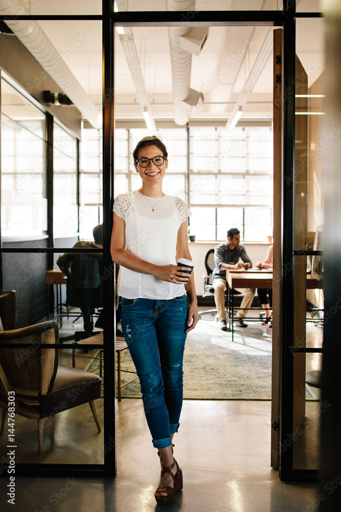Young woman at office doorway holding a coffee Young woman at office doorway holding a coffee