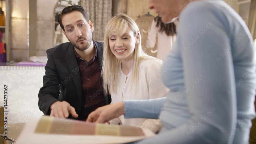 Couple with sales assistant, looking at fabrics in home furnishings store Couple with sales assistant, looking at fabrics in home furnishings store