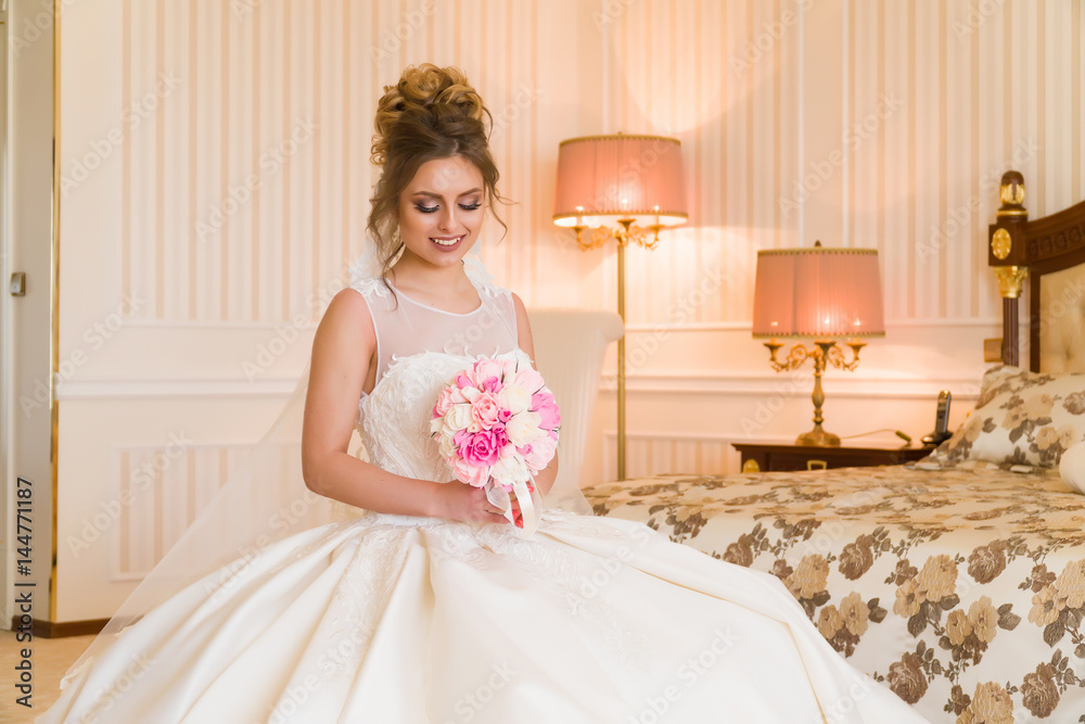 Portrait of beautiful young bride. A girl is posing in a hotel room. A lady is sitting with a bouquet of roses by the window. bride waiting in hotel Portrait of beautiful young bride. A girl is posing in a hotel room. A lady is sitting with a bouquet of roses by the window. bride waiting in hotel