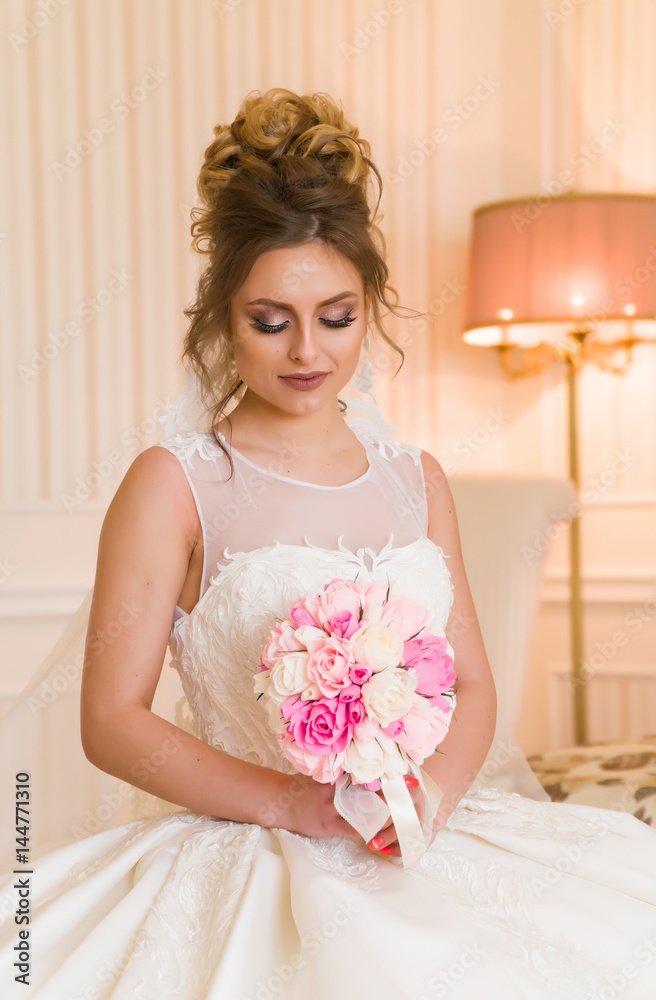 Portrait of beautiful young bride. A girl is posing in a hotel room. A lady is sitting with a bouquet of roses by the window. bride waiting in hotel