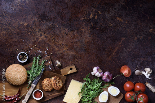 Fresh homemade burger on dark serving board with beef, tomatoes, cheese and eggs over dark background. Top view, copy space.