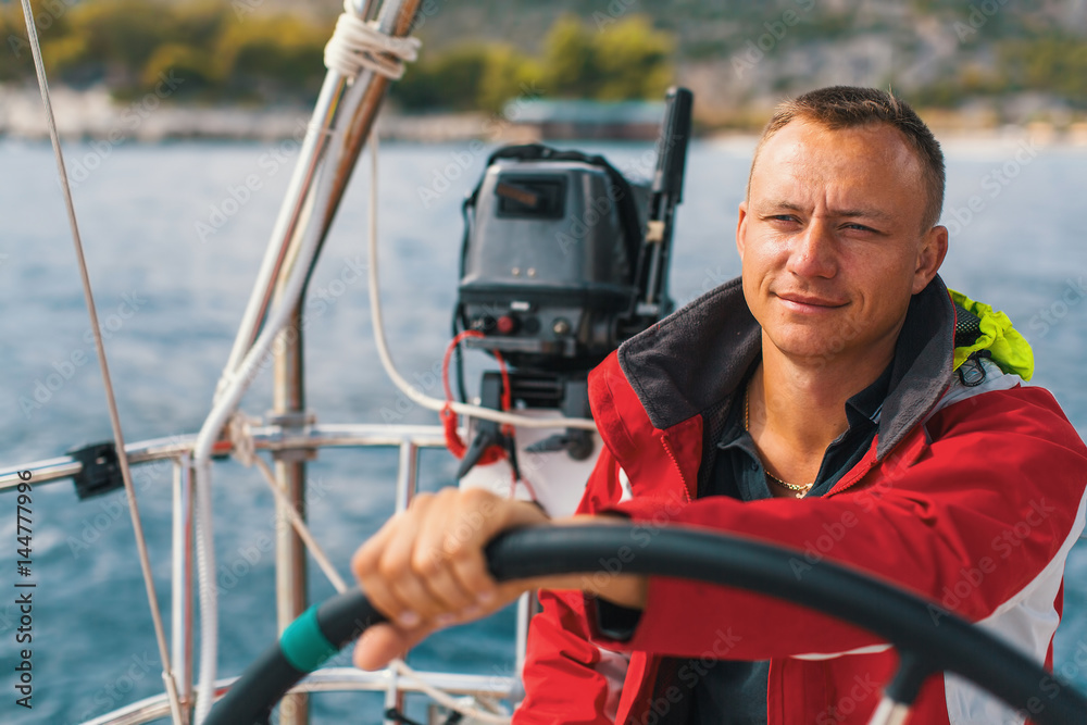 Fototapeta premium Happy sailor at the helm of his sailing yacht.