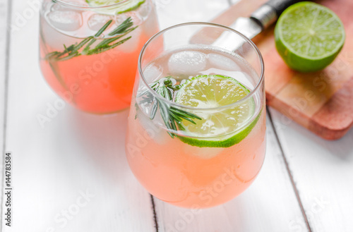 sliced lime, rosemary and natural juice in glass on white table background