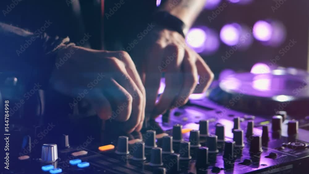 Close-up. Hands of DJ tweak various track controls on DJ mixer console at nightclub party. 4K.
