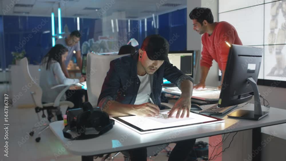  Young creative computer game designer working with colleagues in dark office.