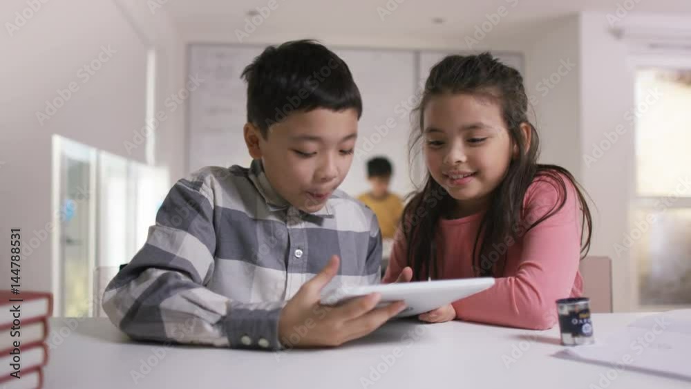 Happy little boy & girl working on computer tablet in school classroom Happy little boy & girl working on computer tablet in school classroom