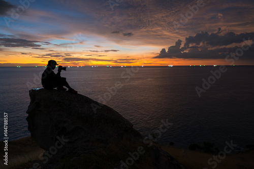 Silhouette of a man photographer sits and looks at the camera,on mountain from the view point Phuket southern of Thailand at Beautiful sunset time