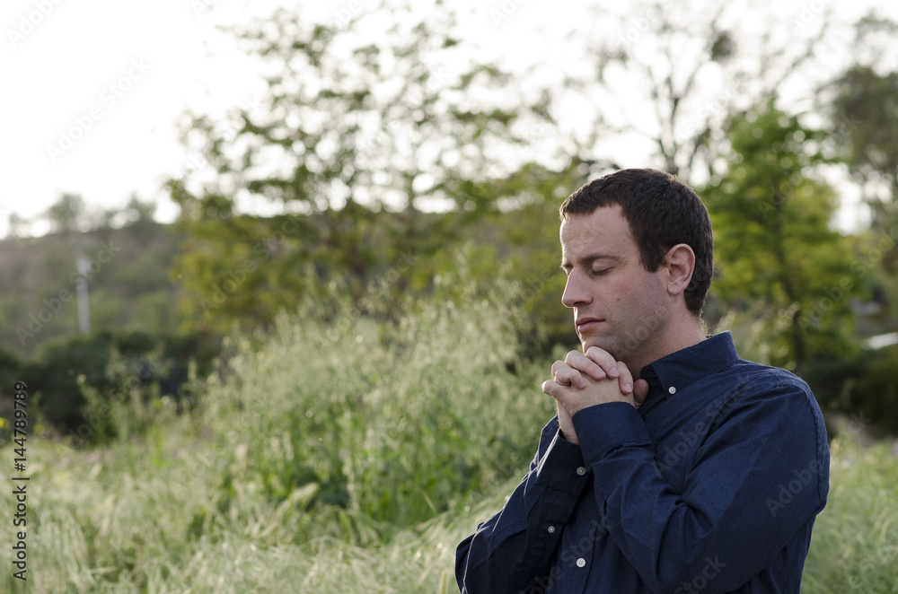 Married man praying outdoors in a grassy field with hands clasped up to his chin. Married man praying outdoors in a grassy field with hands clasped up to his chin.