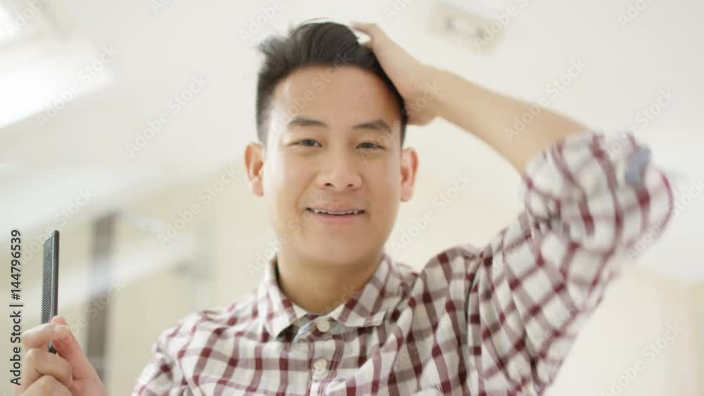 Cheerful young Asian man combing his hair & looking in mirror Cheerful young Asian man combing his hair & looking in mirror