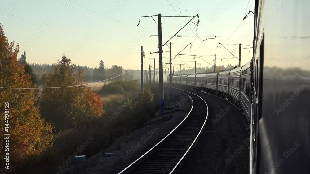 The passenger train is moving along the railway in the forest. A large wagon in the foreground. Bright early autumn sun shines the blue sky. Sunset. Beautiful 4k video The passenger train is moving along the railway in the forest. A large wagon in the foreground. Bright early autumn sun shines the blue sky. Sunset. Beautiful 4k video