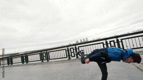 Acrobatic teenager performing acrobatics flips and somersault at promenade - cap flies from his head - stedycam slow-motion photo