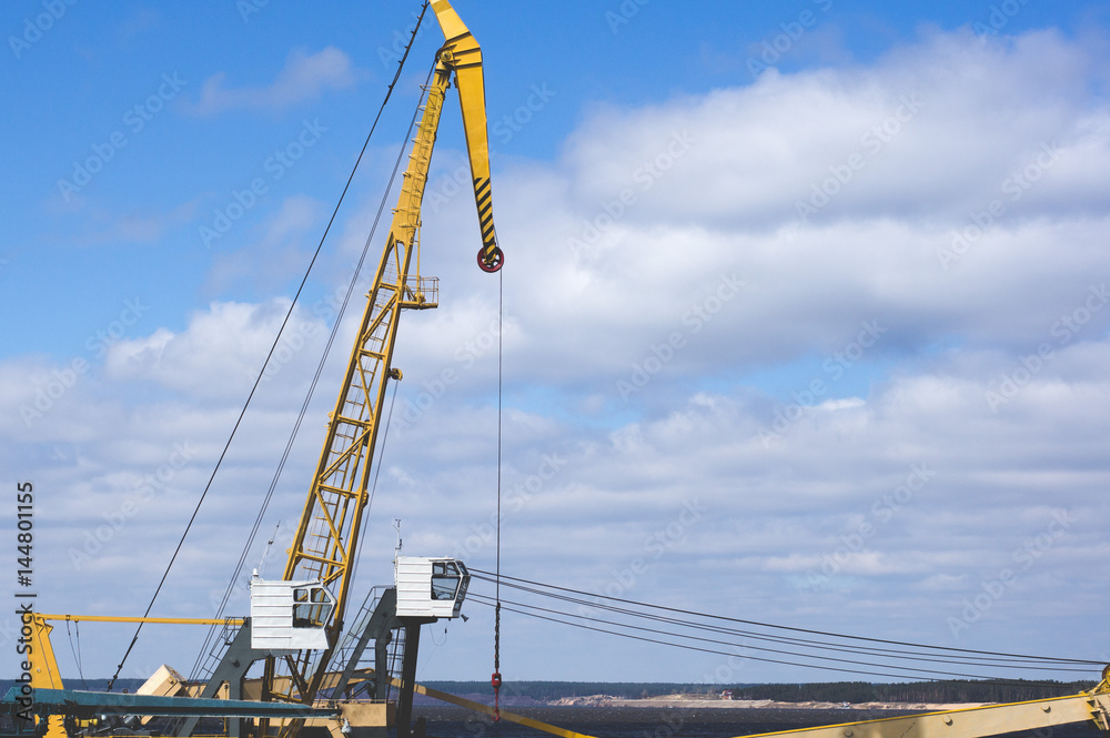 Port crane with yellow arrow against the blue sky and clouds. River port equipment for unloading ships and barges Port crane with yellow arrow against the blue sky and clouds. River port equipment for unloading ships and barges