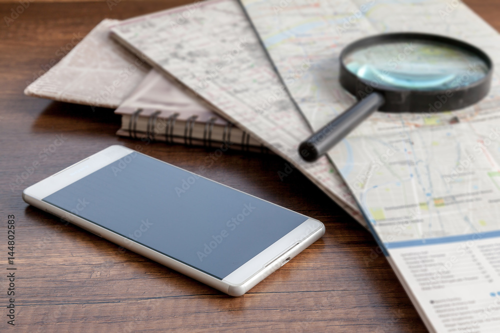 Smartphone, maps and magnifier on wooden table