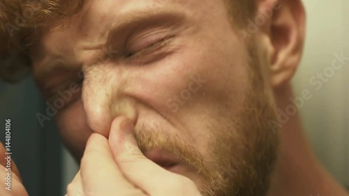 The face of the ill man with blond curly hair and runny nose, coughing. Close-up portrait