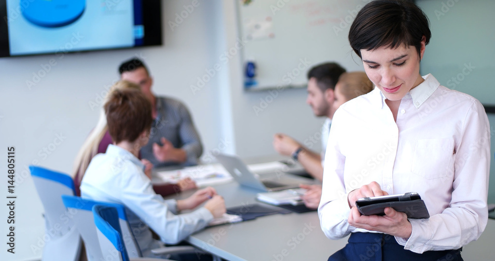 Portrait of smiling casual businesswoman using tablet with coworkers standing in background Portrait of smiling casual businesswoman using tablet with coworkers standing in background