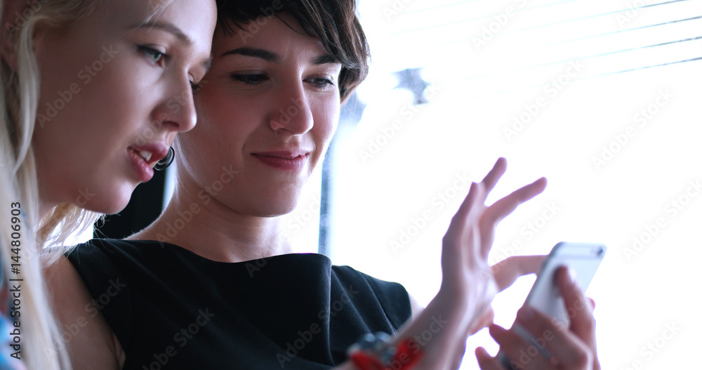 two attractive business women with a cell phone discuss business two attractive business women with a cell phone discuss business
