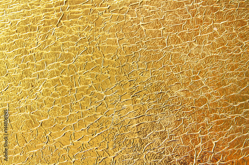 Shiny yellow crumpled leaf gold foil texture background. Bright golden foil backdrop with wrinkles craquelure.