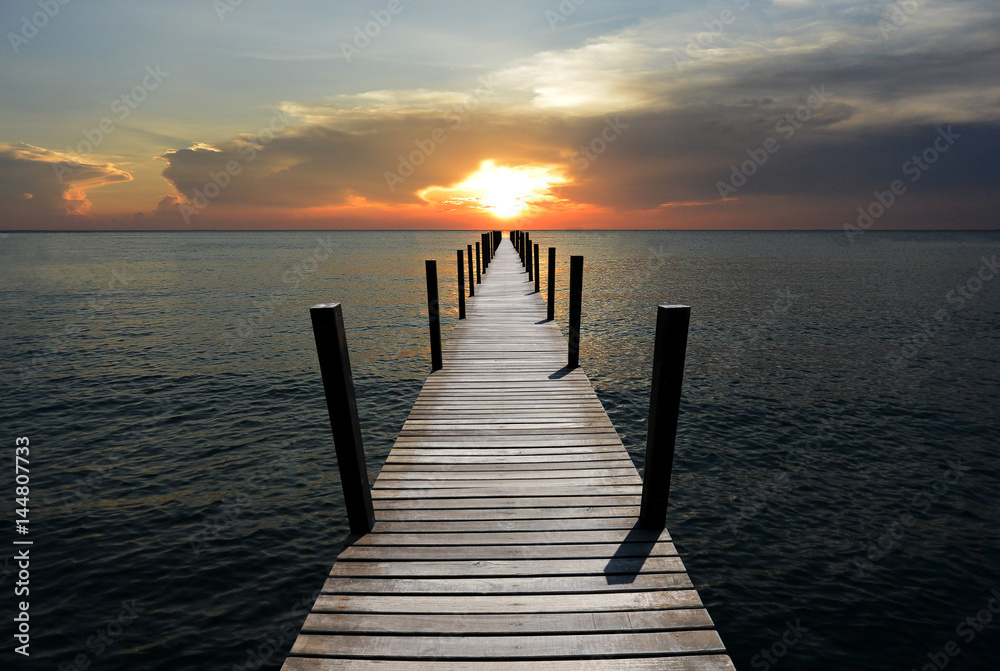 The wooden bridge in the sea at sunset is beautiful.