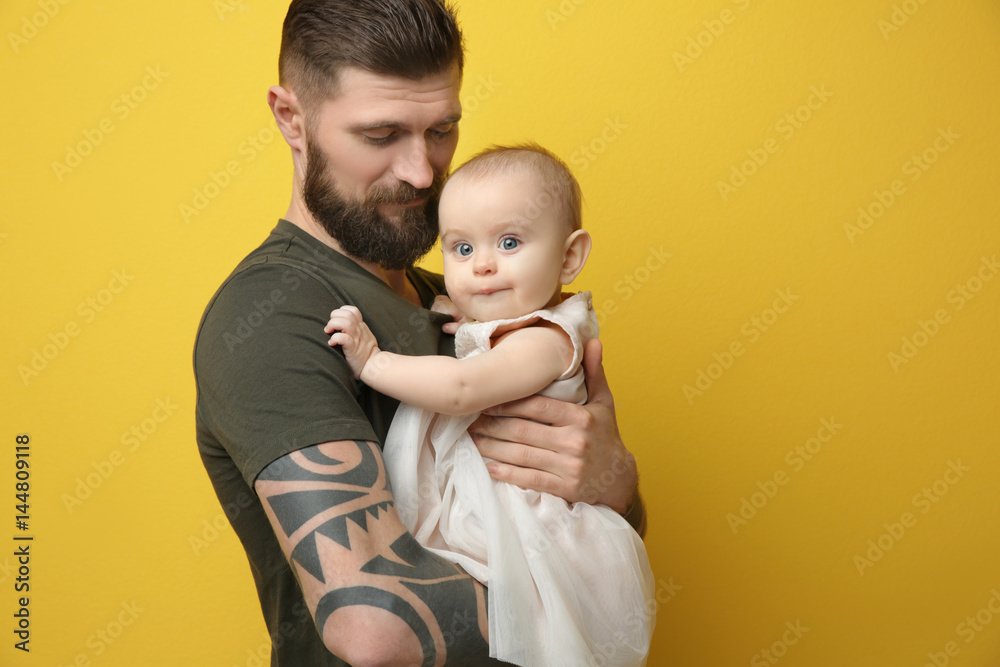Handsome tattooed young man holding cute little girl on color background Handsome tattooed young man holding cute little girl on color background