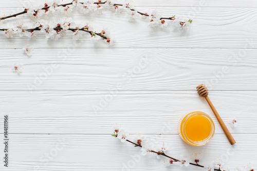Bank of honey, spoon and blossom branches on a white wooden background.