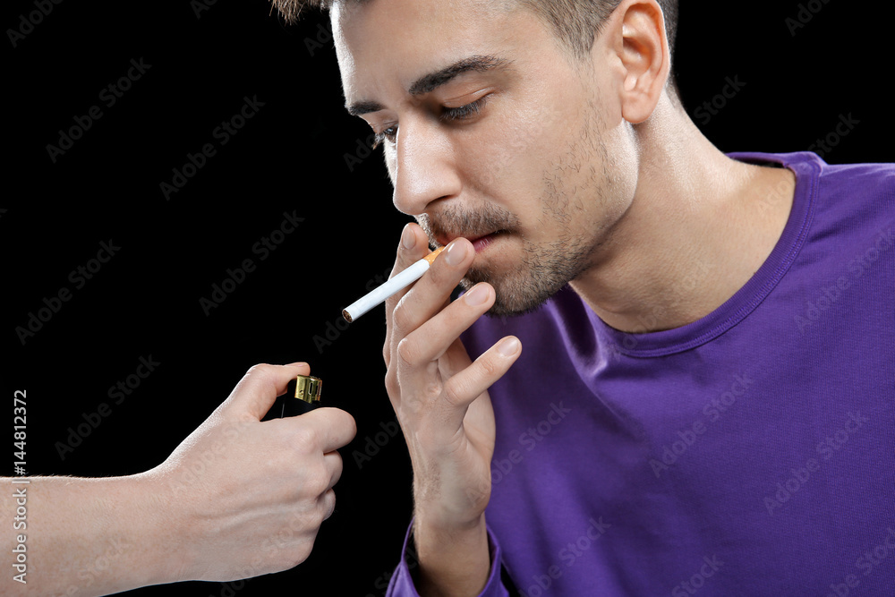 Obraz premium Young man lighting cigarette on black background