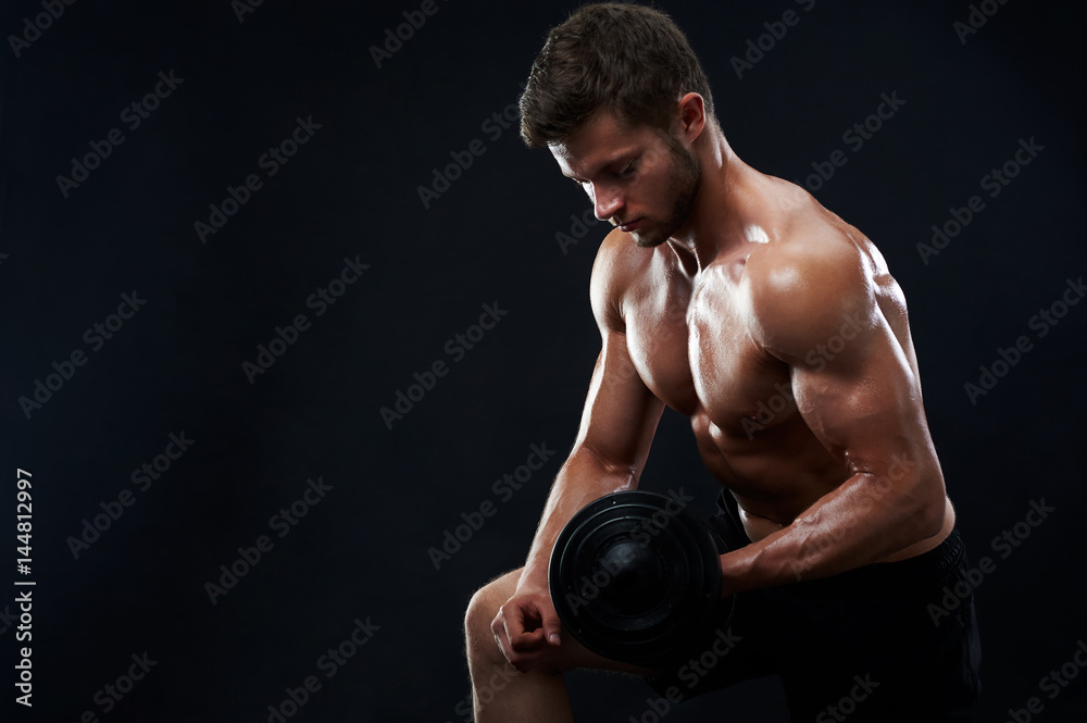 Handsome young shirtless athletic man with perfect sexy hot strong body lifting weights exercising with dumbbells on black background copyspace fitness toning shaping healthy lifestyle sport gym.