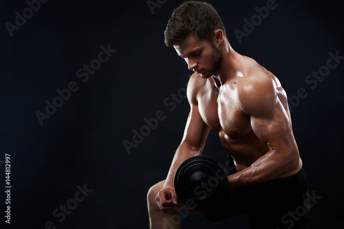 Handsome young shirtless athletic man with perfect sexy hot strong body lifting weights exercising with dumbbells on black background copyspace fitness toning shaping healthy lifestyle sport gym. © serhiibobyk