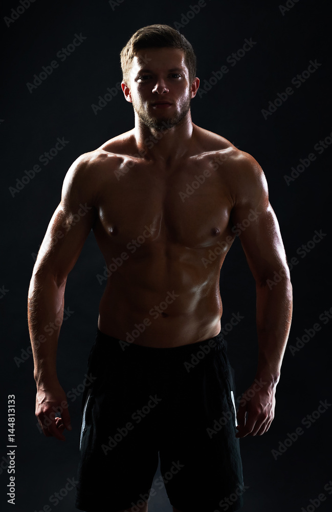 Vertical studio shot of a silhouette of a muscular male athlete posing shirtless on black background fitness gym anonymous mysterious incognito sportsman lifestyle confidence concept.