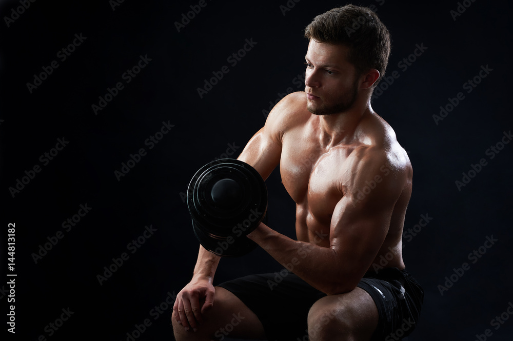 Handsome young sportive shirtless man with muscular strong sexy body doing exercises using dumbbell against black background copyspace gym athletics physique sports motivation achievement gaining.