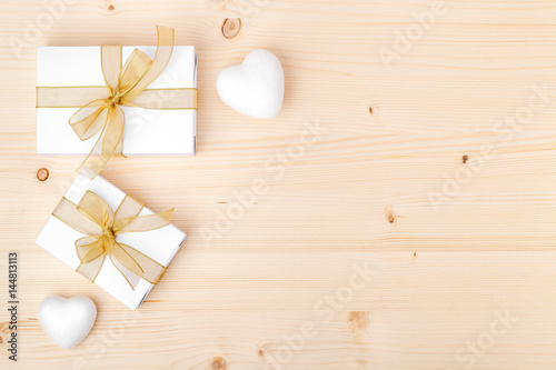 holiday and celebration composition. presents or gifts with gold ribbon and white hearts on wooden background with copy space for text. wedding or anniversary concept. flat lay. top view