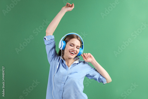 Beautiful young woman in headphones listening to music on color background