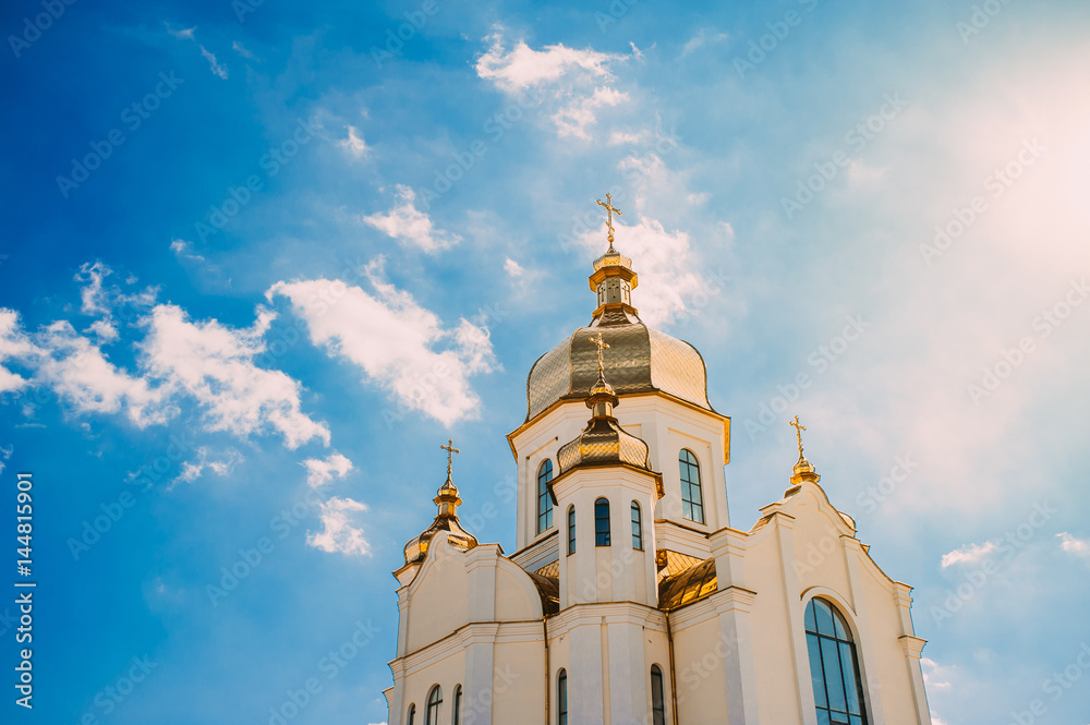 White church with golden domes against a blue sky with clouds.
