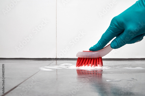 Male hand with red brush cleaning the bathroom tiles on the floor.