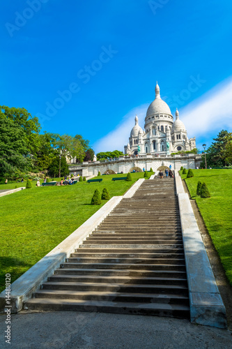 Платно Sacre Coeur Basilica in Paris at day with blue bright sky and green grass and blooming trees