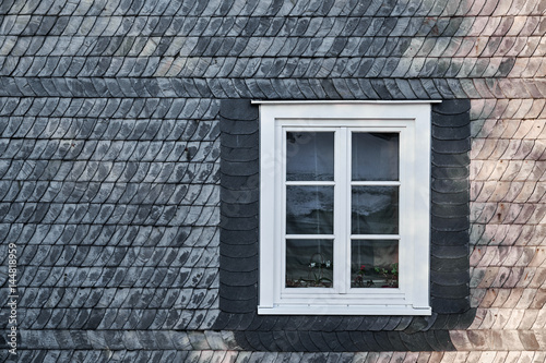 White casement window with mullions, fastened in a black building facade made of slate shingles photo