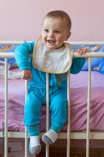 Cute happy baby sitting and smiling in crib