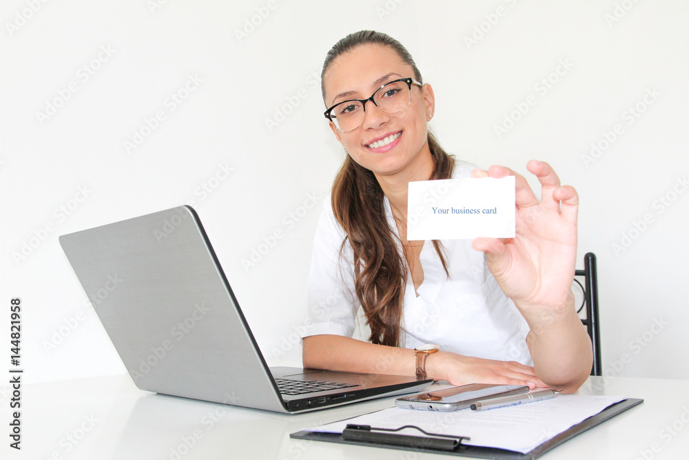 A young woman doctor with a laptop in her office holds a business card A young woman doctor with a laptop in her office holds a business card