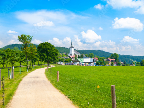 Summer landscape with lush green meadow, country road and white rural church. Prichovice, Northern Bohemia, Czech Republic, Europe. photo