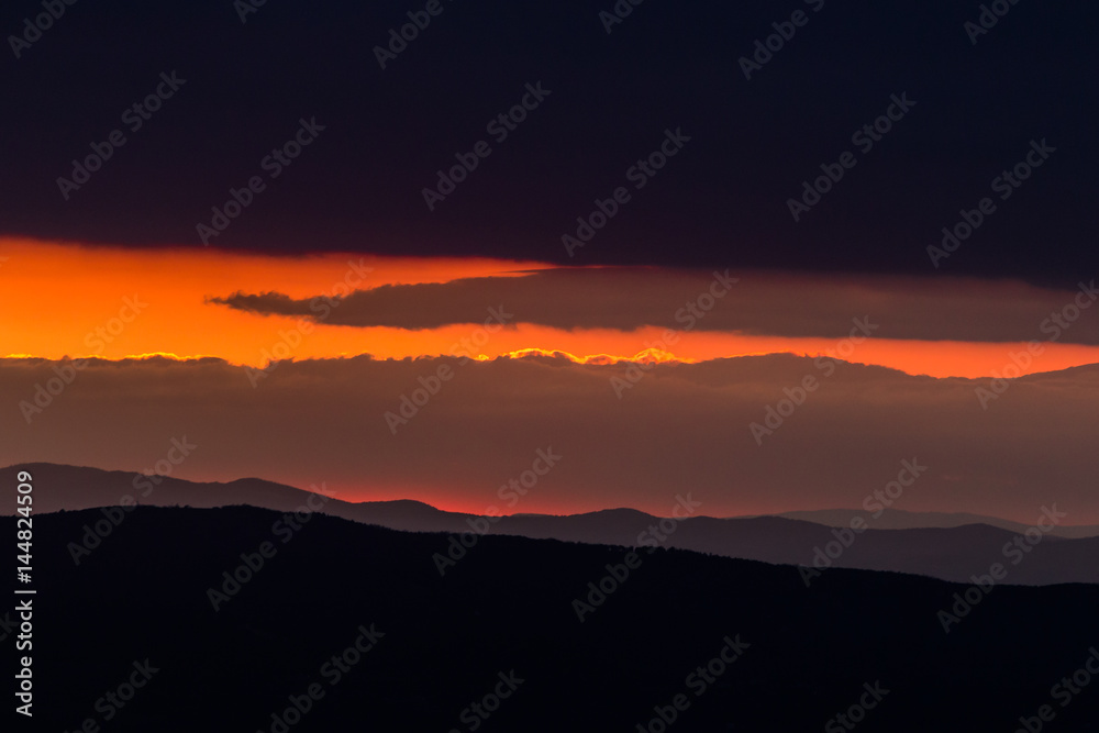 A sunset framed between some dark mountains and clouds, creating an oblique stripe