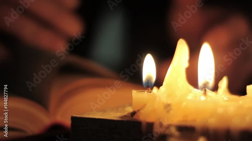 Monk reading and touching a yellow pages of old book. Close-up candle light.