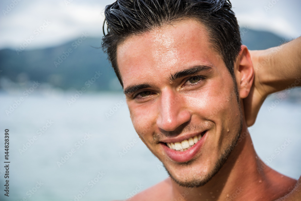 Attractive young man in the sea getting out of water with wet hair, looking  in camera wiht a smile Stock Photo | Adobe Stock