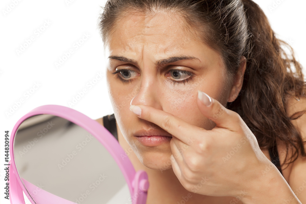 young woman checking her nose with her fingers in front of the mirror young woman checking her nose with her fingers in front of the mirror