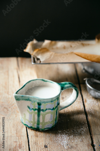 Handcrafted creamer in checkerboard pattern with nilk on wooden background with copy space. Rustic concept. photo