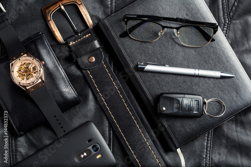 Men's accessories with wallet belt pen car keys glasses smartphone agenda and watch on black leather background.