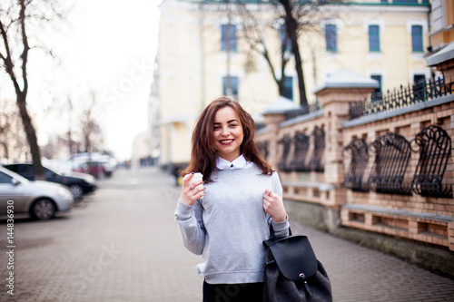 Close up fashion street style portrait of a beautiful girl in a casual outfit walks in the city . Beautiful brunette Keeps coffee.