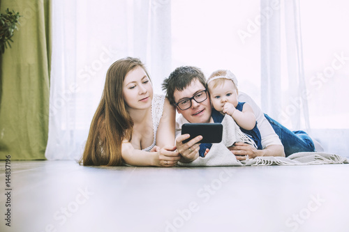 Family mom, dad and baby are doing selfie on phone lying on the floor