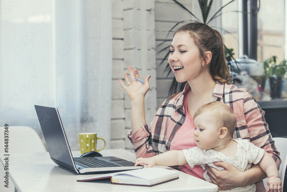 Family mother works with a laptop via the Internet and the baby happy together at home Family mother works with a laptop via the Internet and the baby happy together at home