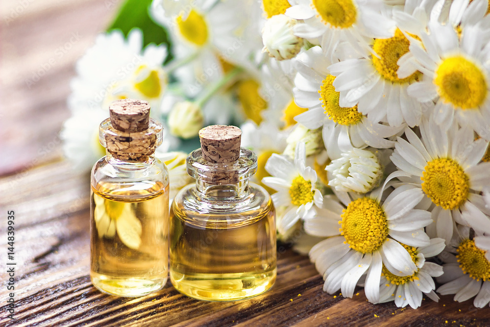 Essential oil in glass bottle with fresh chamomile flowers, beauty treatment. Spa concept. Selective focus. Fragrant oil of chamomile flowers, macro on wooden table horizontal.  - obrazy, fototapety, plakaty 