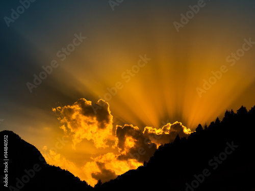 Sun rays shining from behind the cloud. Sunset time with mountail silhouettes. photo